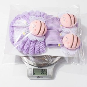 Detail view of purple knitted baby hat and socks set weighing 82.3g on a scale