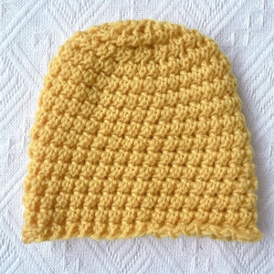 Close-up of bright yellow chunky knit baby hat with thick honeycomb texture pattern