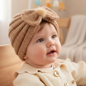 Detailed close-up of a warm khaki baby knitted turban hat with a large bow and fur pompom
