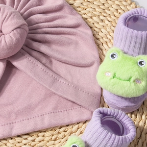 Close-up of pink cotton knot baby hat and purple ribbed socks with plush frog details