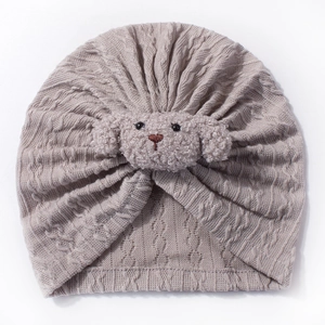 Macro detail of oatmeal knitted baby turban hat with a cute plush puppy decoration