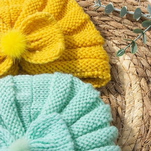 Detail of chunky knit baby hat with large bow and pom-pom decoration in yellow