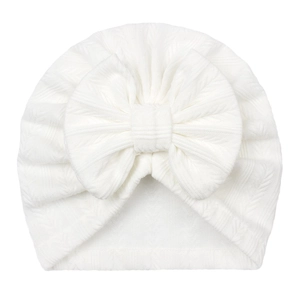 Détail du turban pour bébé avec un grand nœud et une texture de tricot torsadé blanc