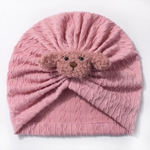 Detail of baby pink turban hat featuring cozy cable knit texture and plush dog ornament