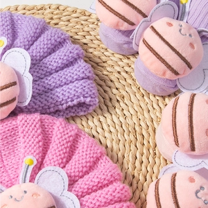 Close-up of baby knit hat featuring a plush pink bee decoration on soft purple yarn