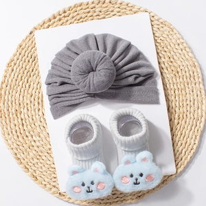 Detail of grey donut knot baby hat and white ribbed socks with blue plush animal faces
