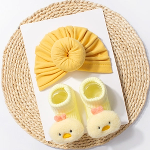 Detail of soft yellow baby turban hat and 3D cartoon duck socks set on woven mat