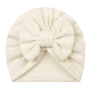 Détail du bonnet turban bébé montrant le tricot jacquard blanc crème et le grand nœud