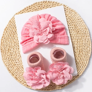 Detailed view of pink knitted baby hat and socks set featuring large 3D floral decorations