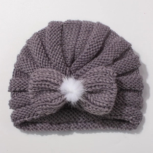 Detail of knitted baby turban hat with bow and white faux fur pompom in dusty pink