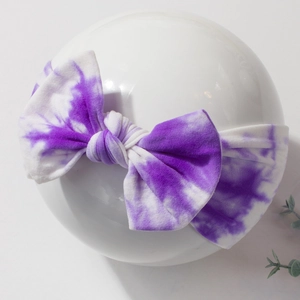 Detail view of purple tie-dye nylon bow headband for infants on a display prop