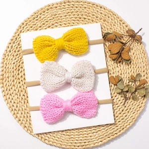 Three-pack elastic baby headbands with colorful knitted bows on a rustic display