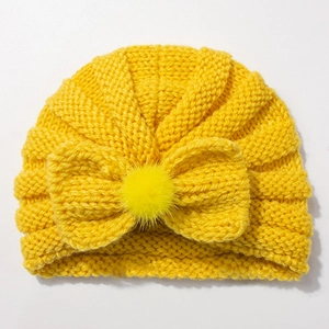 Close-up of mustard yellow knit baby turban with a large bow and soft faux fur pom-pom