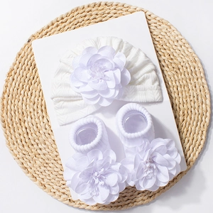 Detailed view of white newborn hat and socks set featuring large 3D silk flower accents