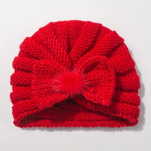 Detail of red knit baby turban hat with a large bow and soft faux fur pom-pom