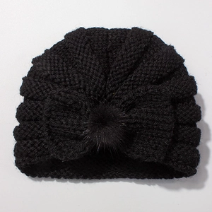 Detailed close-up of a black knit baby turban hat with a large bow and faux fur pompom