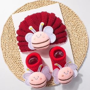 Detail of red knitted baby hat and socks set featuring cute plush bee decorations