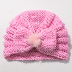 Detail showing pink knit baby hat with ribbed texture and decorative bow with faux fur pom