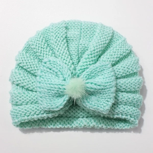 Detailed knit texture of mint green baby hat with bow and decorative pom-pom