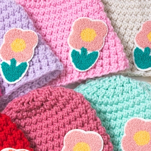 Close-up of knit baby beanies featuring 3D floral embroidery and soft crochet texture