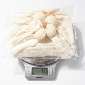 Detail showing baby flower hat weight of 43.6g on a scale in clear packaging