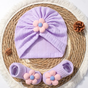 Newborn purple knitted baby hat and socks set with 3D floral accents on a rustic mat