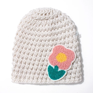 Detailed view of handmade cream crochet knit baby hat with pink flower embroidery patch