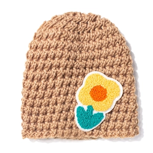 Detailed knit texture of light brown baby hat featuring yellow crochet flower ornament