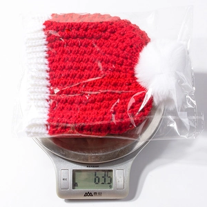 Weight measurement of red and white knit Christmas baby hat with white faux fur pompom