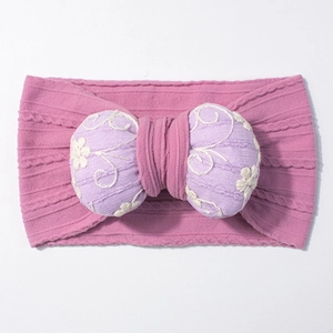 Detailed close-up of stretchy knit baby headband with embroidered purple bow and floral patterns