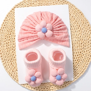 Detailed view of pink knitted baby turban hat and matching flower socks on a straw mat