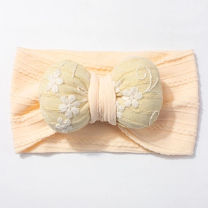 Detail of baby headband featuring soft ribbed pink fabric and embroidered yellow bow