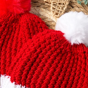 Close-up of red and white knit baby hat featuring fluffy faux fur pompom and thick texture