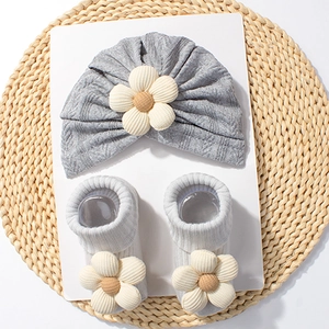 Detail view of gray baby knit hat and socks set with 3D floral accents on woven background