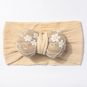 Detail of baby headband with white flower embroidery on a soft beige knit bow