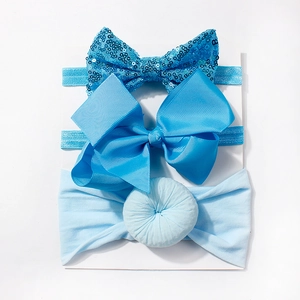 Detailed view of three blue baby headbands with sequins and bows on a white card
