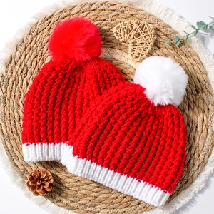 Winter baby knit hat set in festive red with fuzzy pom-poms on rustic straw background