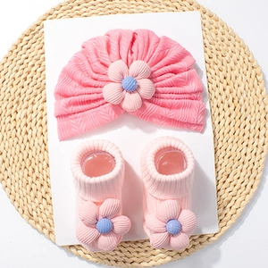 Close-up of pink knit baby hat and socks set featuring large 3D fabric flower details