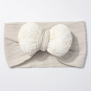Detail of baby headband featuring soft cream knit fabric and lace floral bow decoration