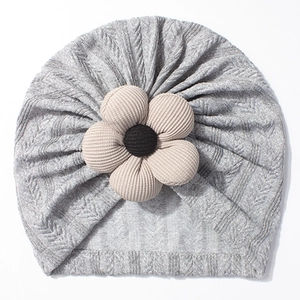 Close-up of grey knit baby beanie featuring a beige corduroy flower and braided texture