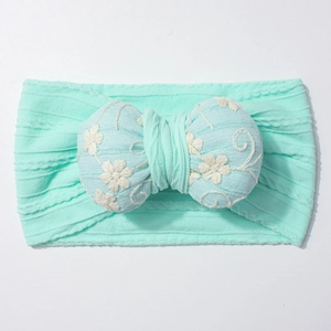 Macro shot of mint green elastic baby headband with blue floral embroidered bow detail