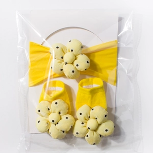 Detail von gelbem Baby-Stirnband und Socken-Set mit gepunkteter Blume in Verpackung
