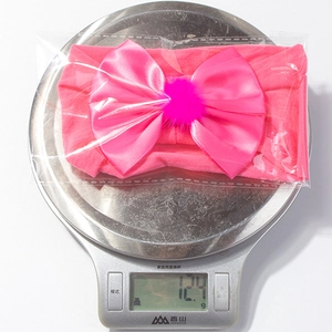 Vue détaillée du bandeau pour bébé rose avec nœud pesant 12,4g sur une balance précise