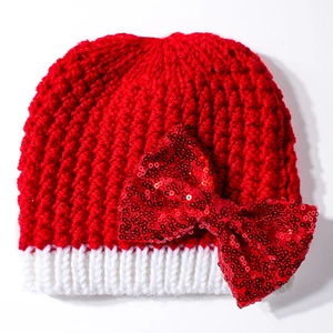 Detailed close-up of a red knitted baby Christmas hat with a large red sequin bow detail