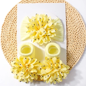 Detail of yellow baby headband and socks set with large floral accents on woven mat