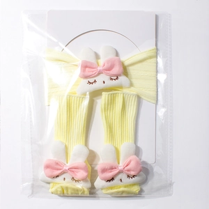 Detail view of yellow baby headband and sock set with cute rabbit dolls in plastic packaging