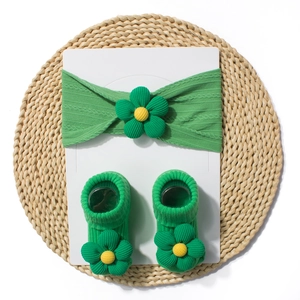Detailed shot of green baby headband and socks set with 3D floral accents on white card