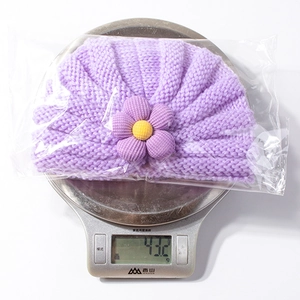 Dettaglio cappello neonato in maglia viola con motivo a onde e decorazione floreale 3D