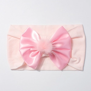 Détail d'un bandeau bébé en nylon rose avec un nœud en satin et un pompon moelleux