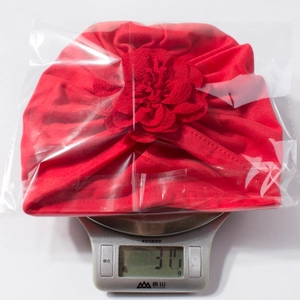 Dettaglio del cappello neonato rosso con fiore dal peso di 31,7g sulla bilancia